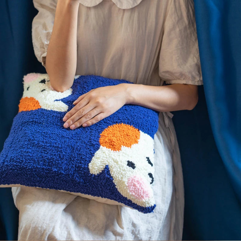 Person holding a colorful pillow with a cartoon character design against a blue curtain background
