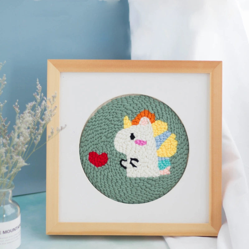 Handmade circular punch needle art of a cute white unicorn with a colorful mane and red heart.