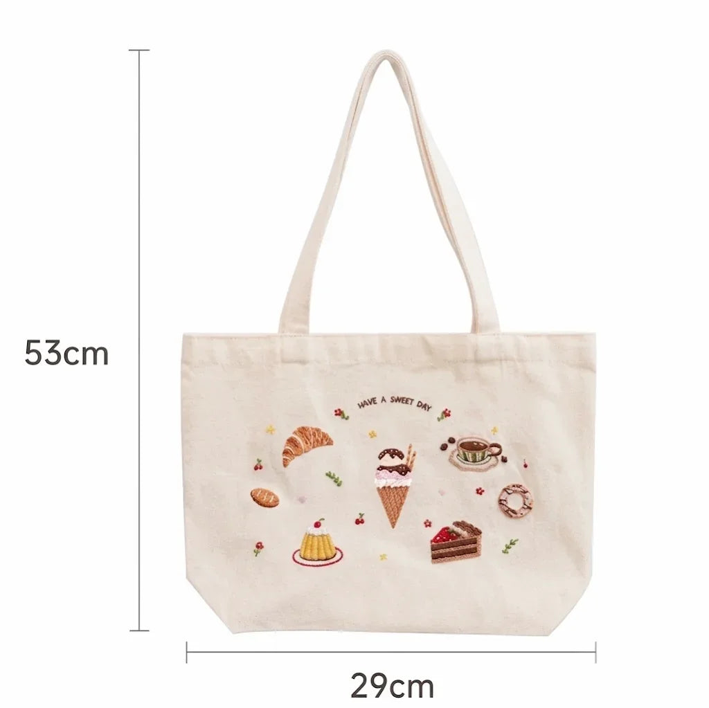 Cream canvas tote bag with embroidered dessert pattern and 'HAVE A SWEET DAY' text.