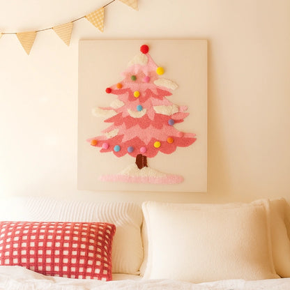 Pink Christmas tree punch needle embroidery kit art on a white wall above a bed.