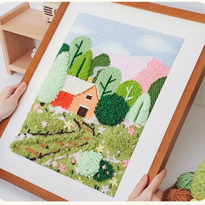 Punch needle embroidery kit featuring a cabin in a green forest landscape.