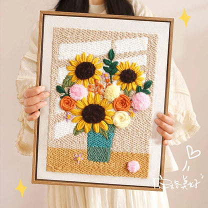 Hand holding a Calivra Craft punch needle kit depicting sunflowers in a teal vase by a window