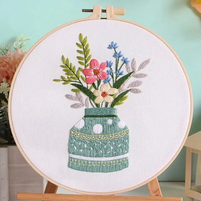 Hand embroidery of colorful flowers in a green vase on white fabric in a wooden hoop.