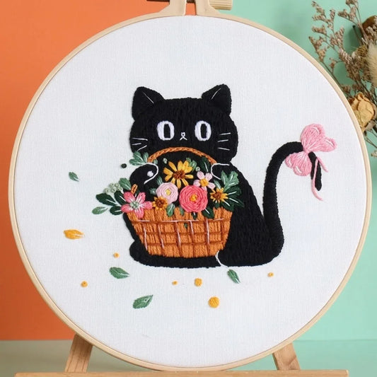 Handmade embroidery hoop art featuring a cute black cat holding a colorful flower basket.