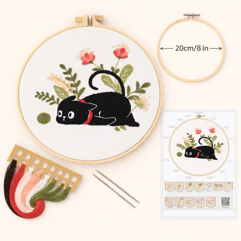 Embroidery hoop with black cat design, floral elements, and embroidery kit on a white background