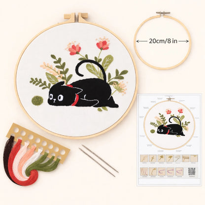 Embroidery hoop with black cat design, floral elements, and embroidery kit on a white background