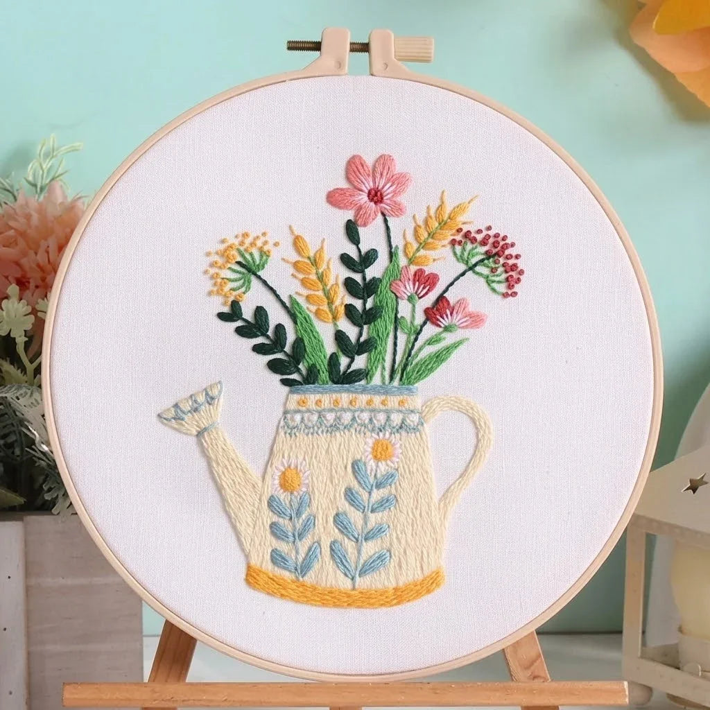 Hand-embroidered floral arrangement in a decorative watering can within a wooden hoop