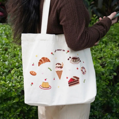 White tote bag featuring dessert DIY embroidery with croissant, ice cream, and cake designs.