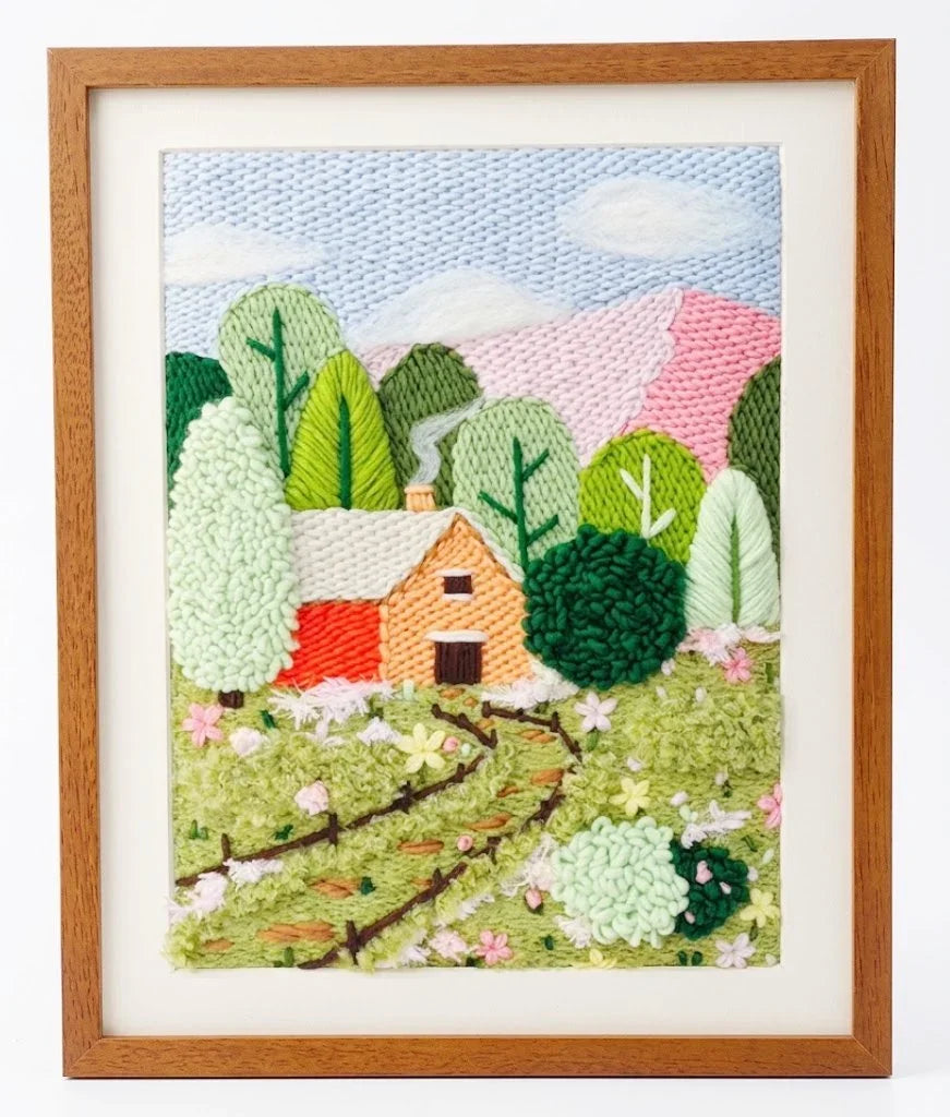 Punch needle embroidery kit featuring a cabin in a forest landscape with mountains and trees.