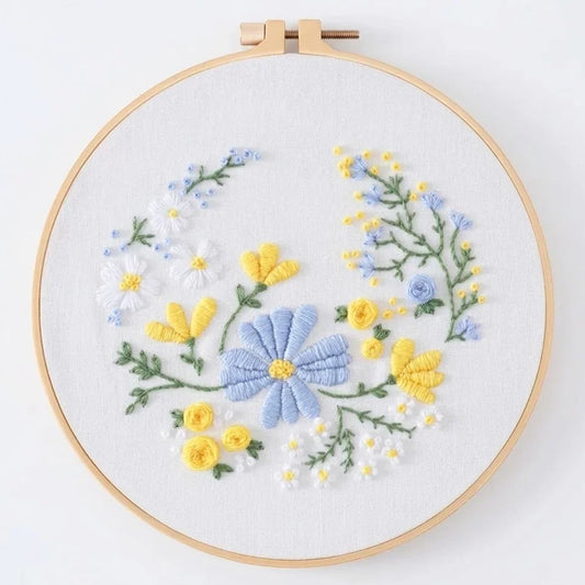 Hand embroidery of blue and yellow wildflowers in a wooden hoop.