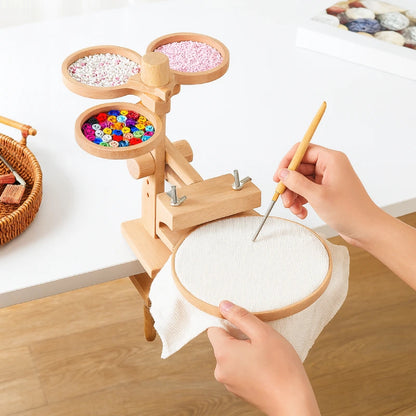 Wooden embroidery hoop with colorful beads and a hand holding a needle on a wooden table.