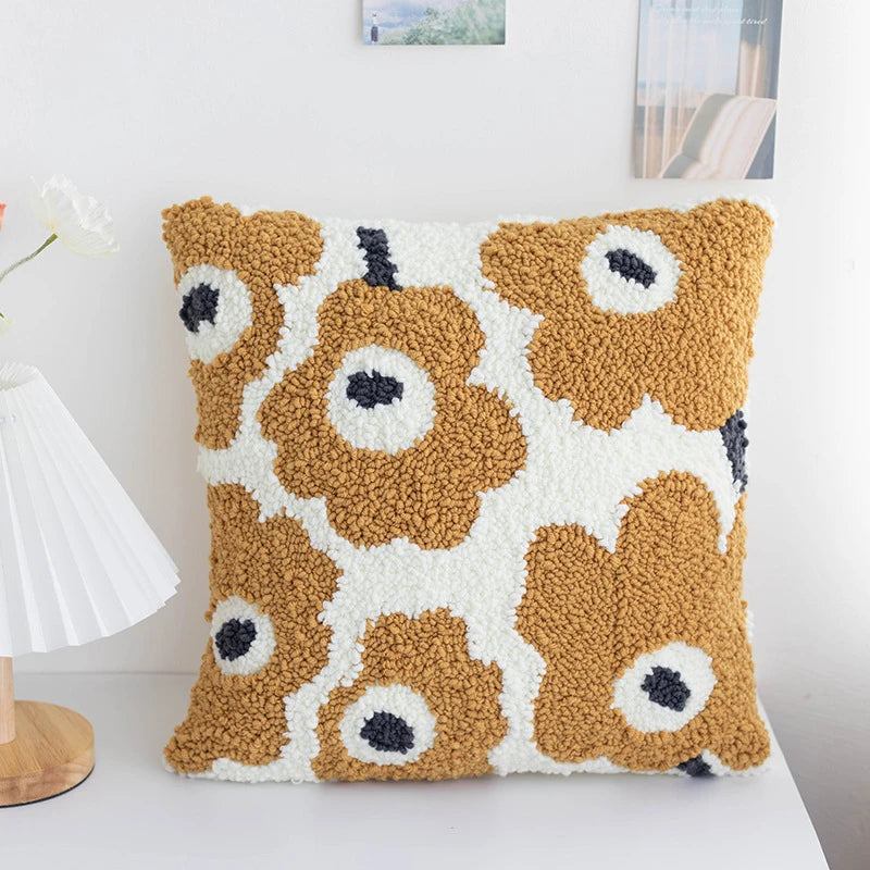 Decorative pillow with brown floral pattern on a white surface.A warm-toned punch needle pillow cover with soft amber flowers and creamy white petals. Its cozy, retro-inspired design brings natural charm and handmade warmth to any room.