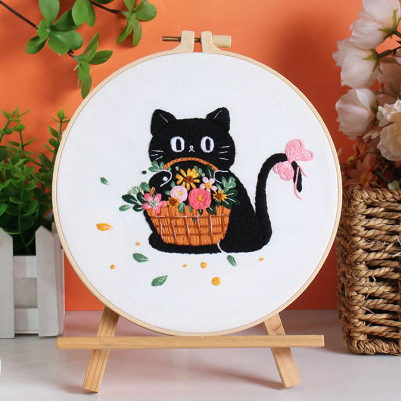 Embroidery hoop with a black cat holding a basket of flowers on an orange background