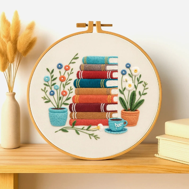 This cozy embroidery design features a charming stack of colourful books surrounded by potted flowers and a small teacup, creating a warm and peaceful reading corner vibe. The rich tones of red, teal, and brown bring a touch of comfort and creativity, perfect for book lovers and home décor enthusiasts alike.
