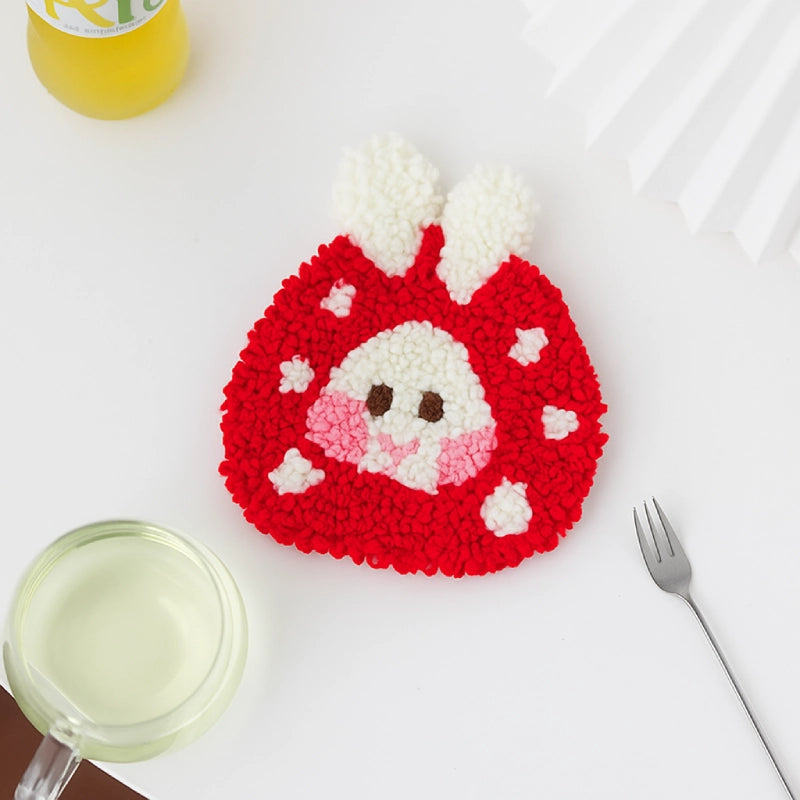 Crocheted red and white animal coaster on a white surface with a glass and fork.