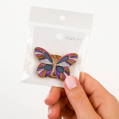 Butterfly-shaped jewelry on a clear packaging with 'Jewelry' label, held by a hand.