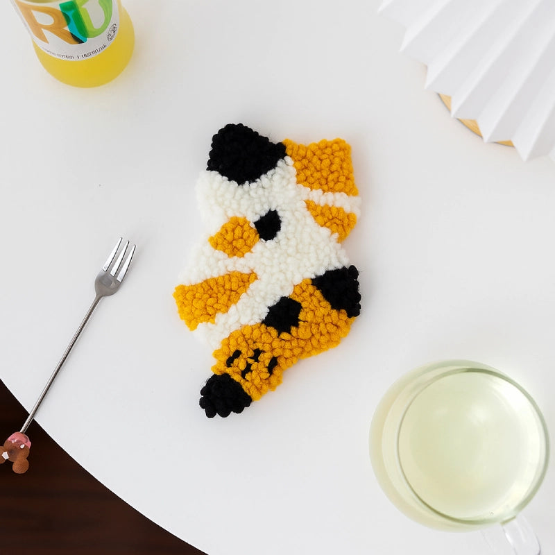 Handmade cat-shaped object made of yellow, black, and white beads on a white surface with a fork and glass.