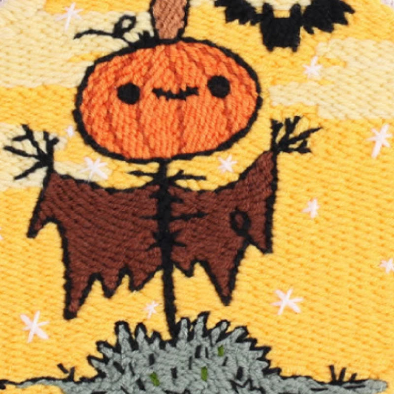 This punch needle design features a cheerful pumpkin-headed scarecrow under a golden Halloween sky, with a playful bat flying nearby. I