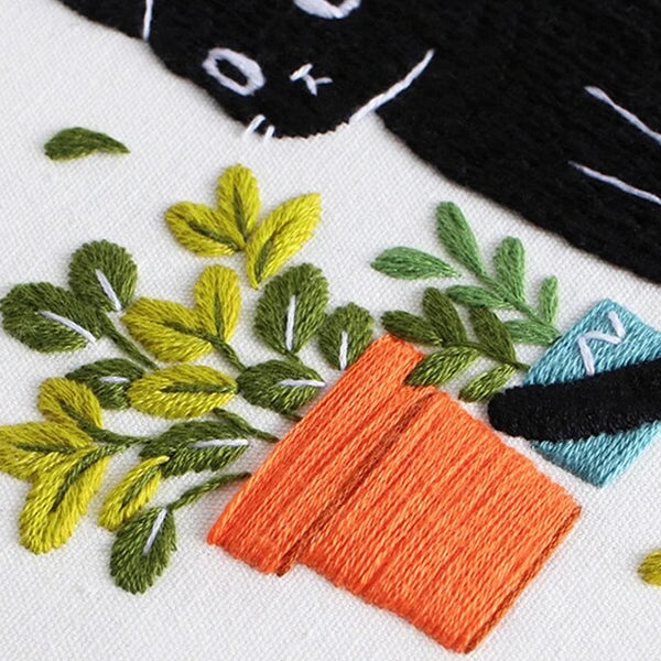 Embroidery design with leaves, carrots, and a cat on a white background