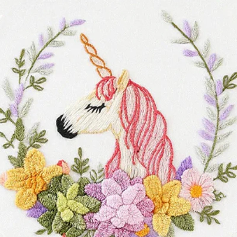 This embroidery design features a graceful unicorn with a soft pink mane and a golden horn, surrounded by a vibrant floral wreath. The mix of yellow, purple, and green blooms creates a harmonious and dreamy atmosphere