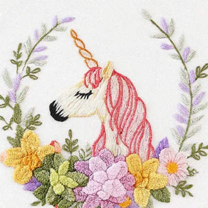 This embroidery design features a graceful unicorn with a soft pink mane and a golden horn, surrounded by a vibrant floral wreath. The mix of yellow, purple, and green blooms creates a harmonious and dreamy atmosphere