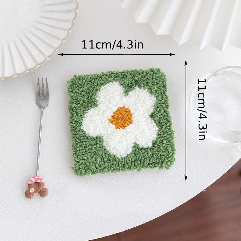 Square green rug with a white flower design, placed on a table with a fork and glass.