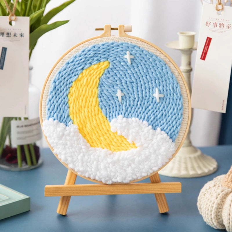 Woven circular art piece with a yellow moon and blue sky on a wooden stand.