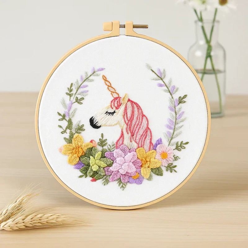 This embroidery design features a graceful unicorn with a soft pink mane and a golden horn, surrounded by a vibrant floral wreath. The mix of yellow, purple, and green blooms creates a harmonious and dreamy atmosphere — perfect for adding a touch of magic and elegance to any space.