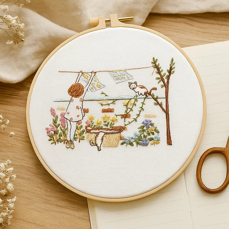 Embroidery hoop with a completed embroidery design of a child and cat by a tree on a wooden surface.