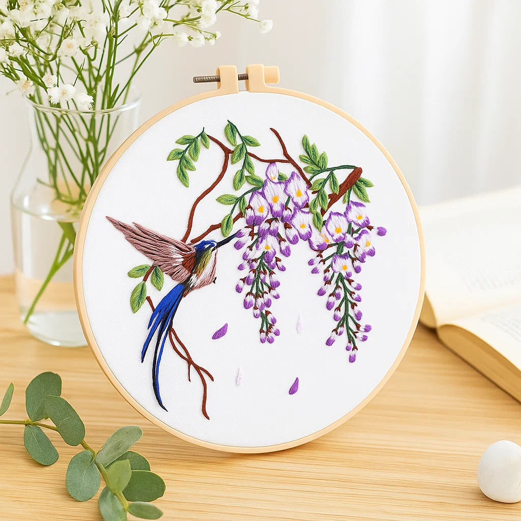Embroidery hoop with a hummingbird and wisteria design on a wooden surface.