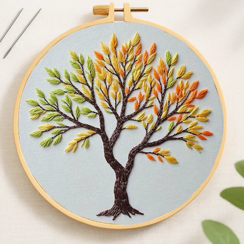 Embroidery hoop with a tree design featuring autumn leaves on a light blue background.