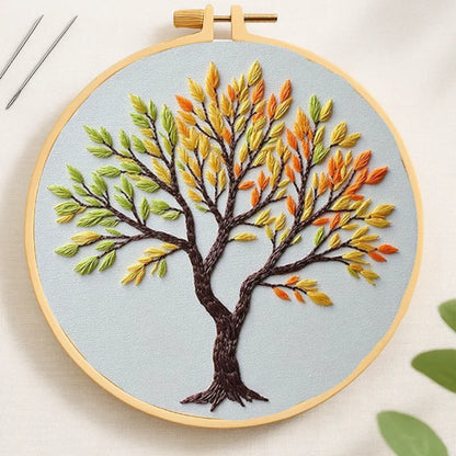Embroidery hoop with a tree design featuring autumn leaves on a light blue background.