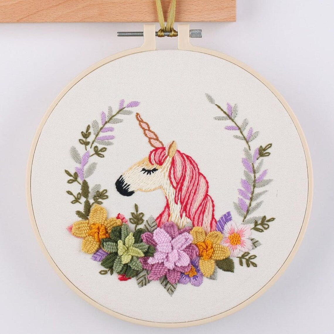 Embroidery hoop with a unicorn design surrounded by flowers on a white background
