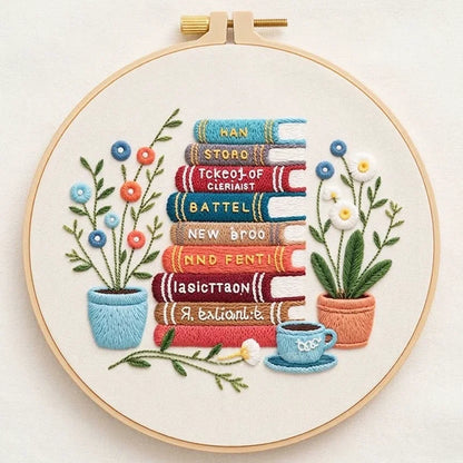 Embroidery hoop featuring a stack of colorful books, potted plants, and a teacup.