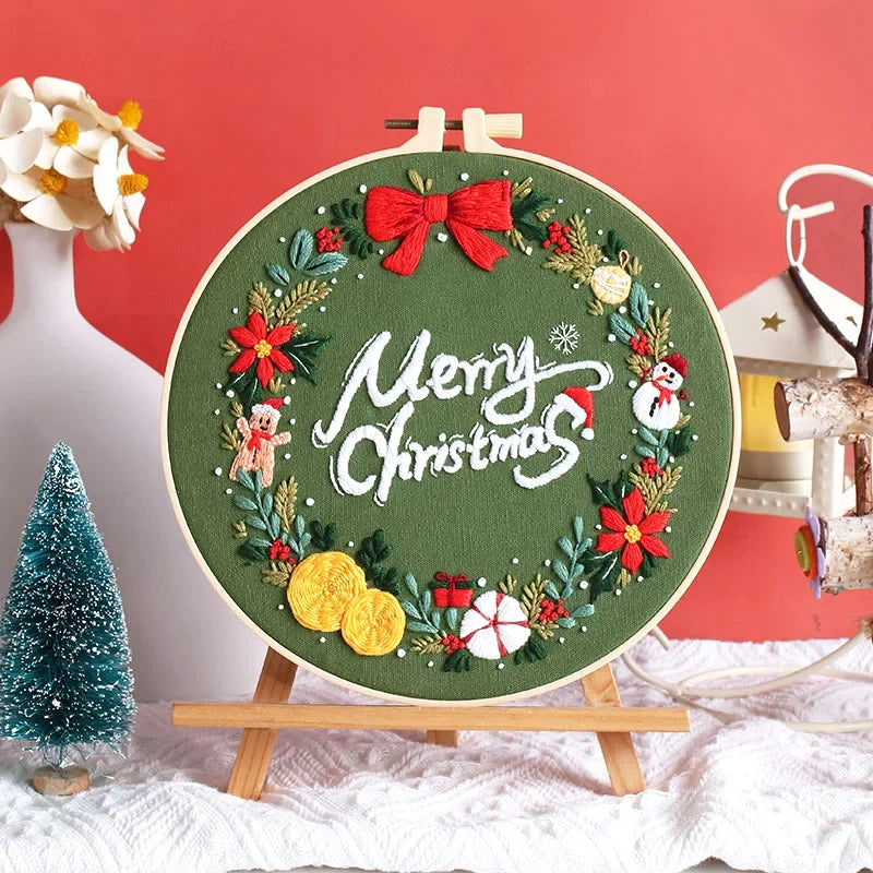 Set on a rich green background, this festive embroidery features a joyful Christmas wreath surrounding the “Merry Christmas” message. Adorned with a red bow, holly leaves, snowman, gingerbread man, and gift boxes, it captures the warmth and cheer of the holiday season. Perfect as a handmade decoration or a thoughtful gift for loved ones.