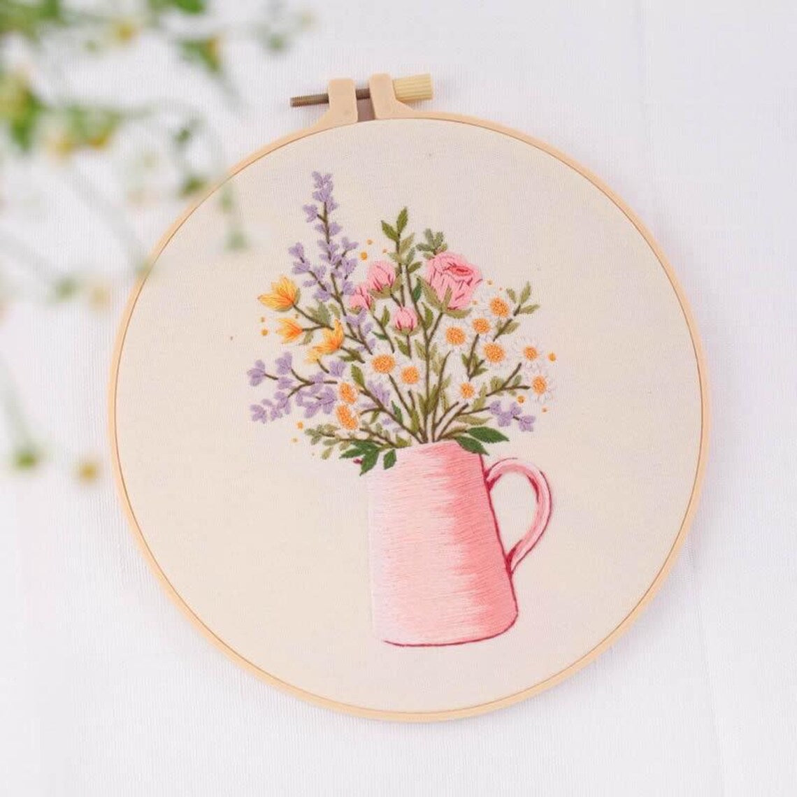 Embroidery hoop with a pink teapot and floral design on a white background