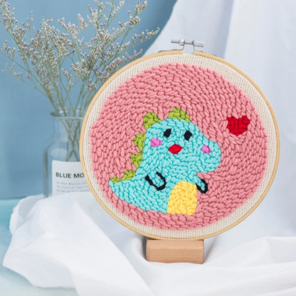 A smiling blue dinosaur with green spikes and a red heart on a pink background.