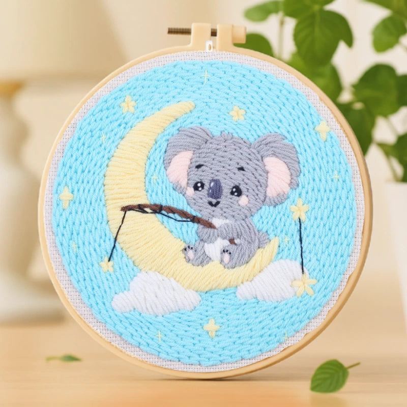 This adorable embroidery design features a cute koala sitting on a crescent moon, holding a fishing rod among twinkling stars. The soft pastel colors of blue, yellow, and gray create a dreamy night-time atmosphere.