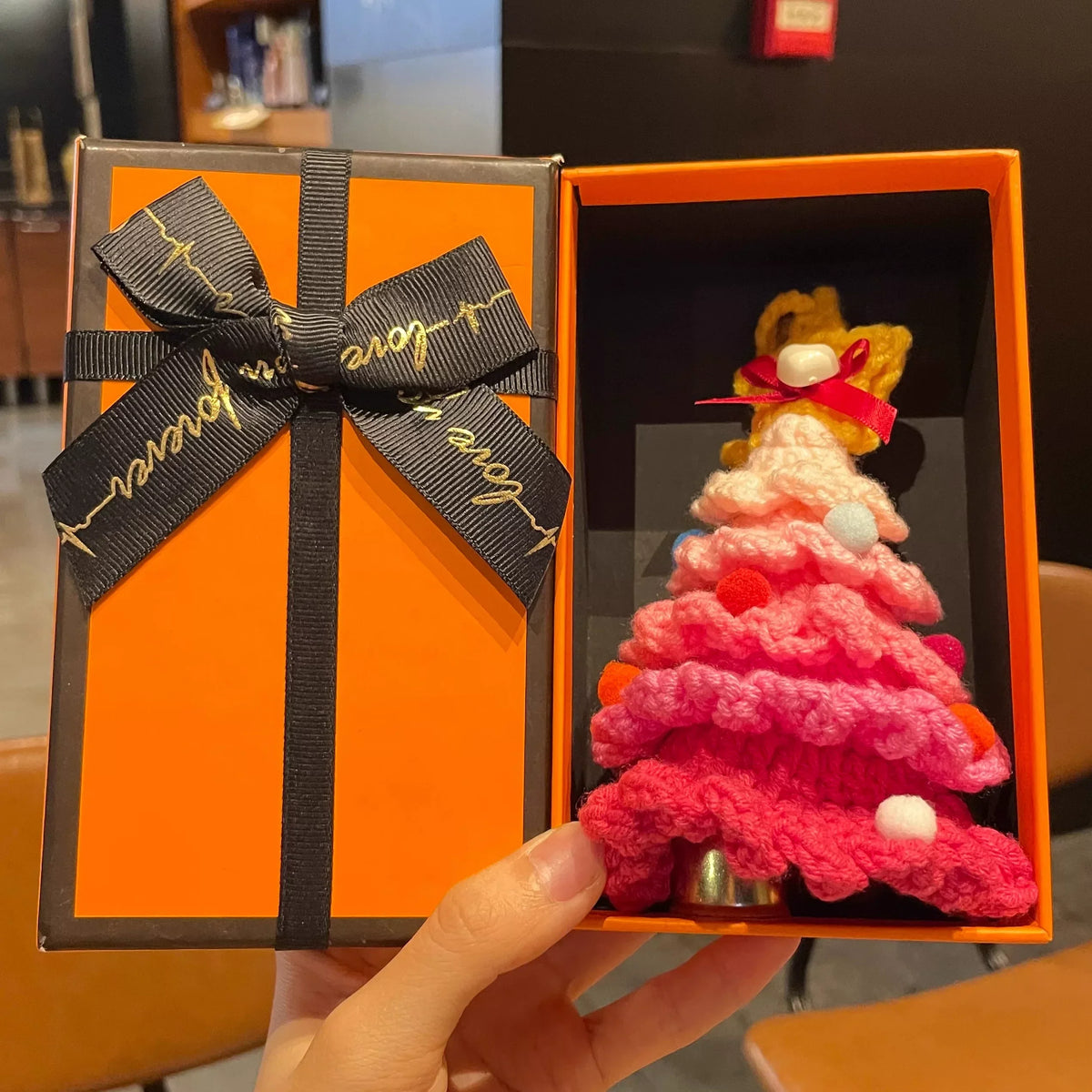 Pink knitted Christmas tree hanging ornament by Calivra Craft in an orange gift box.