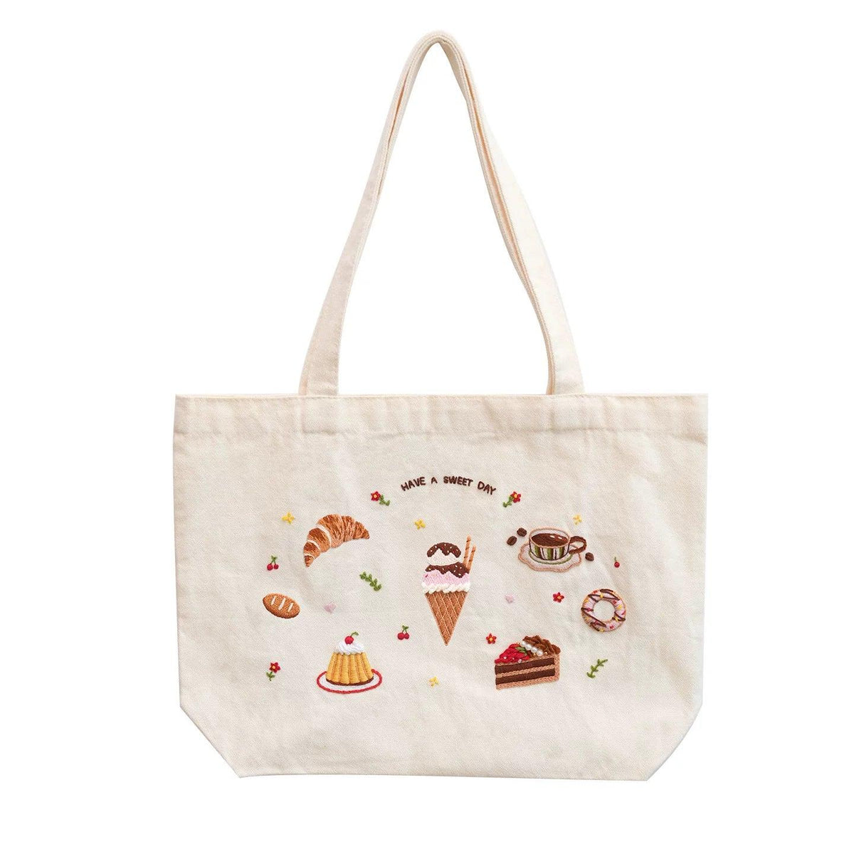 Cream tote bag with embroidered dessert motifs and 'HAVE A SWEET DAY' text.