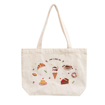 Cream tote bag with embroidered dessert motifs and 'HAVE A SWEET DAY' text.