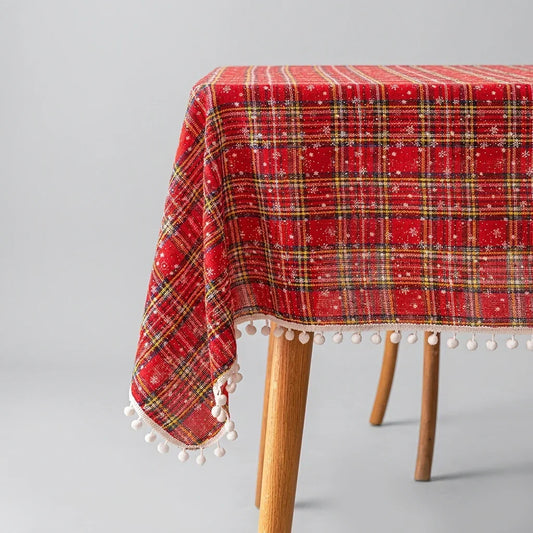 Red Christmas plaid round tablecloth with white pom pom trim on a wooden table.