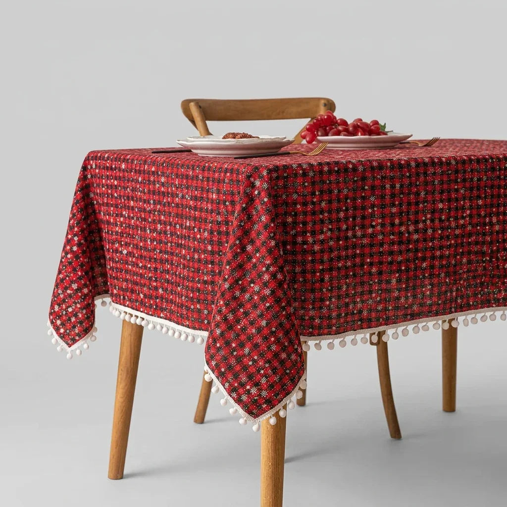 Christmas plaid round tablecloth with white pom-pom trim on a wooden table.