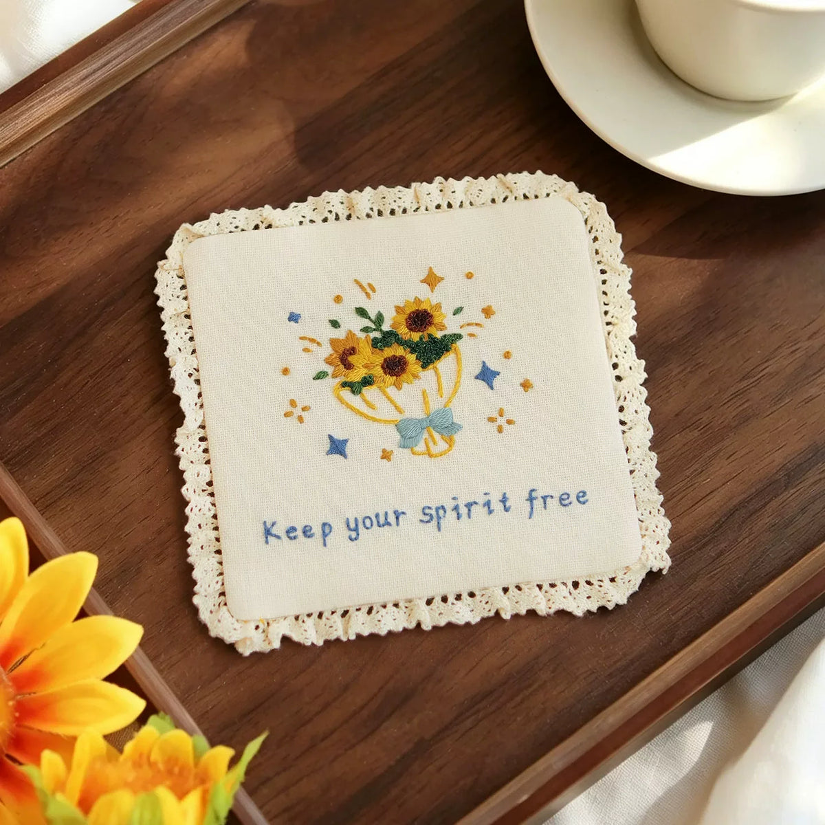 Hand-embroidered cream coaster with yellow sunflowers and 'Keep your spirit free' text.