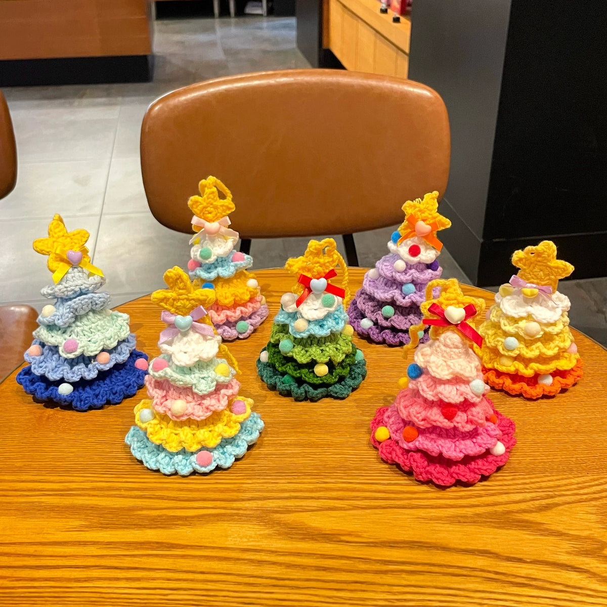 Set of colorful Calivra Craft knitted Christmas tree hanging ornament pendants on a wooden table.