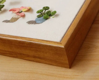 Close-up of 3D green plant and flower embroidery by Calivra Craft in a wooden frame.