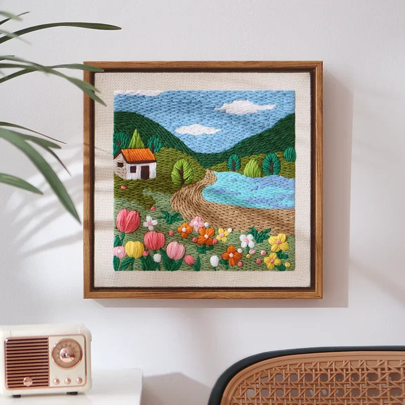 Punch needle embroidery kit featuring a landscape with a house, mountains, and flowers.