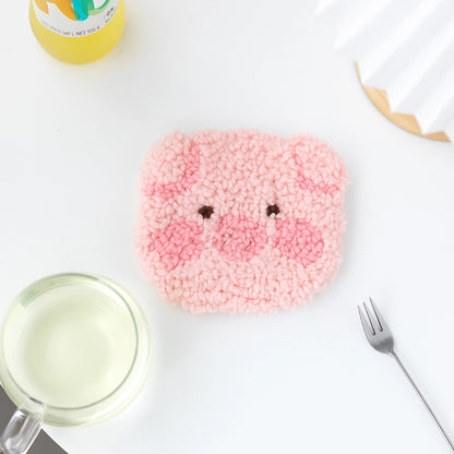 Pink textured square with face-like features on a white surface with a glass of milk and a fork.