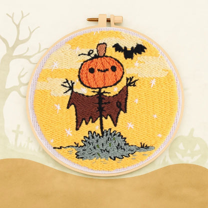 This punch needle design features a cheerful pumpkin-headed scarecrow under a golden Halloween sky, with a playful bat flying nearby.