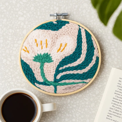 Embroidery hoop with floral design on a textured surface with a cup of coffee and book.